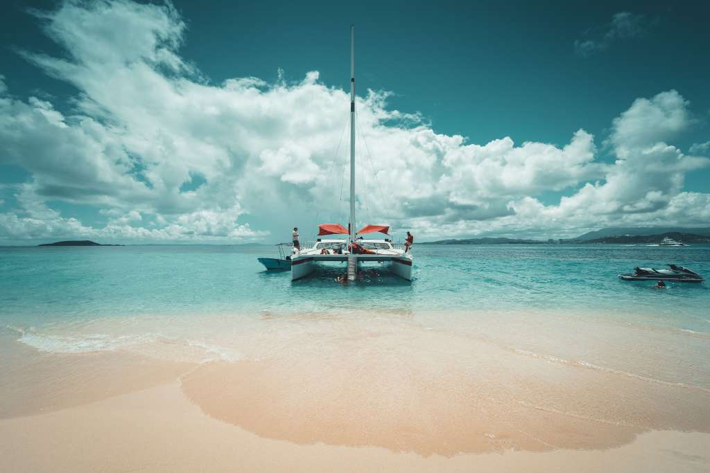 Private catamaran rental in Monaco anchored near a sandy beach, with guests enjoying clear coastal waters and water activities.